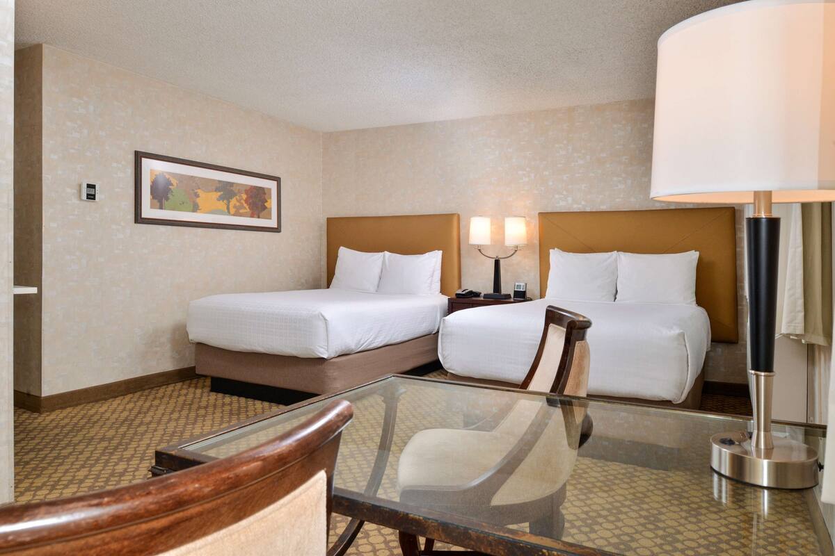 A hotel room with two beds, a glass table, and a chair.