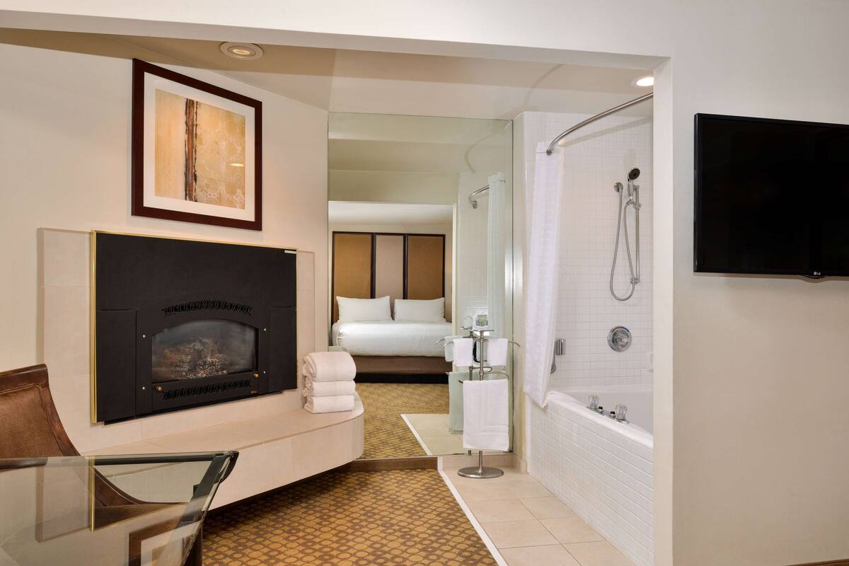 A hotel room with a fireplace, a bed, a shower, and a TV.