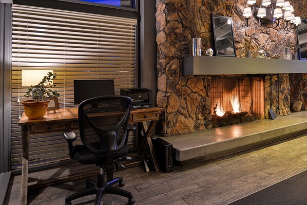 A modern office space with a wooden desk, black office chair, and a fireplace with a stone wall backdrop.