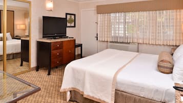 A hotel room with a bed, a television, a dresser, a mirror, and a window with curtains.