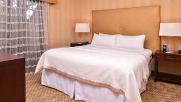A hotel room with a large bed, two bedside tables, a nightstand, a wooden desk, and a patterned carpet.