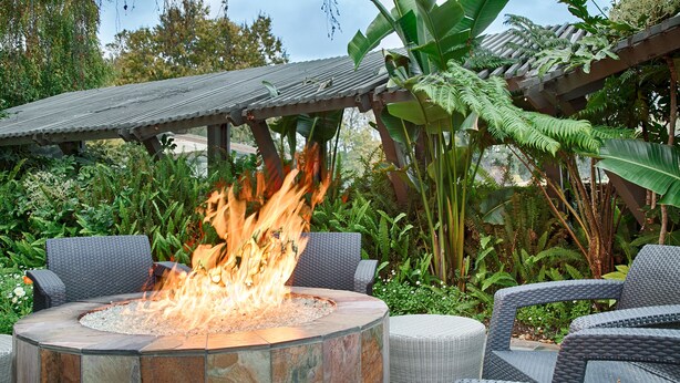 A circular fire pit with seating around it, surrounded by lush greenery and a pergola overhead. - Best Western Corte Madera Inn (Corte Madera)