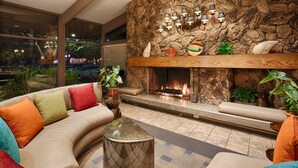 A modern living room with a stone fireplace, a sofa with colorful cushions, and a view of the street outside. - Best Western Corte Madera Inn (Corte Madera)