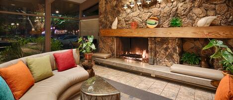 A modern living room with a stone fireplace, a sofa with colorful cushions, and a view of the street outside.