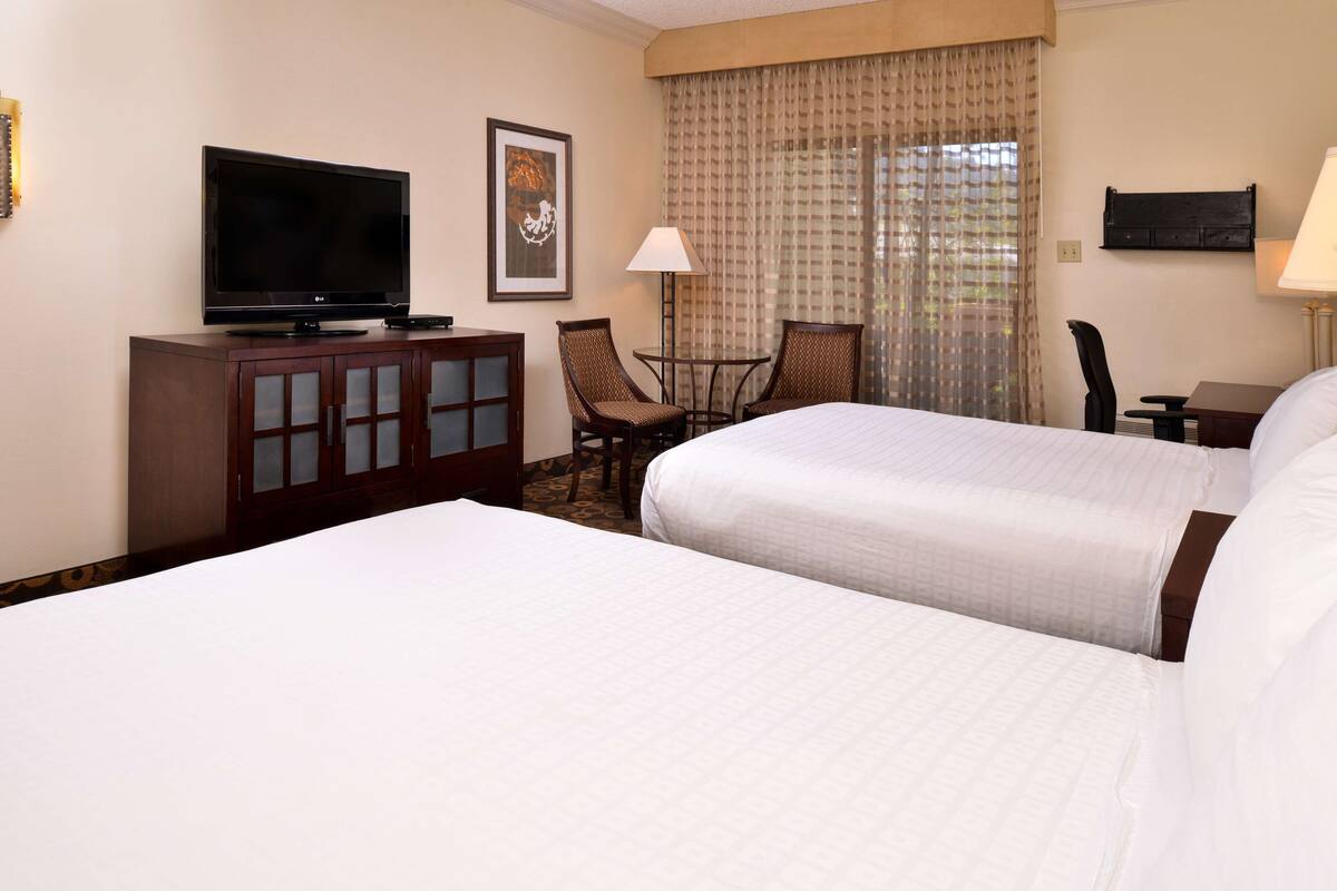 A hotel room with two beds, a TV, a desk, and a chair.