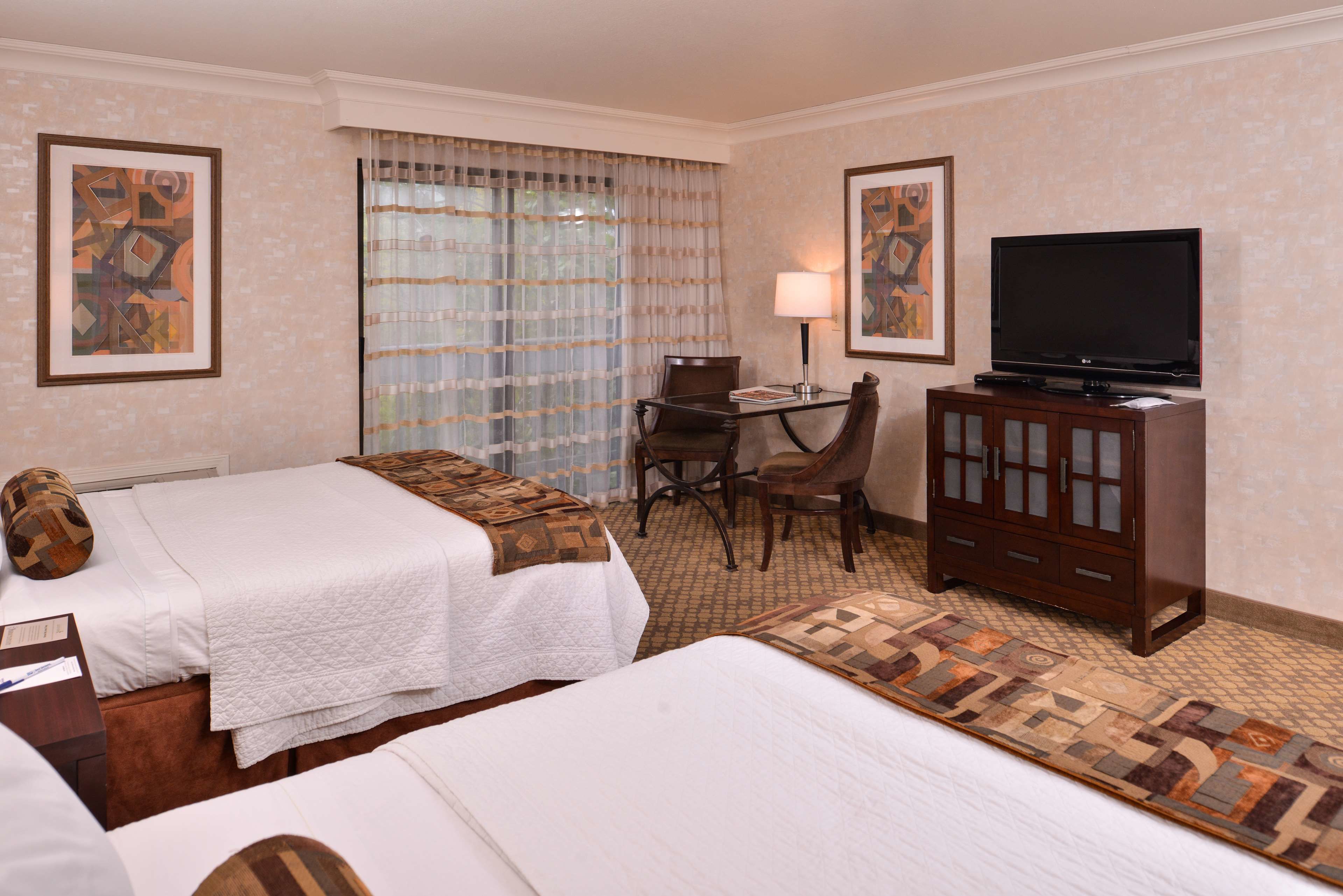 A hotel room with two beds, a desk with a chair, a television, and artwork on the walls.
