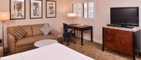 A hotel room with a bed, a desk, a television, a chair, and a sofa.