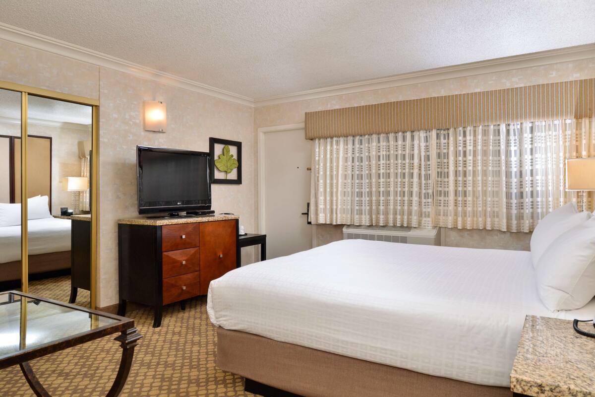 A hotel room with a bed, a television on a dresser, a desk, and a mirror.