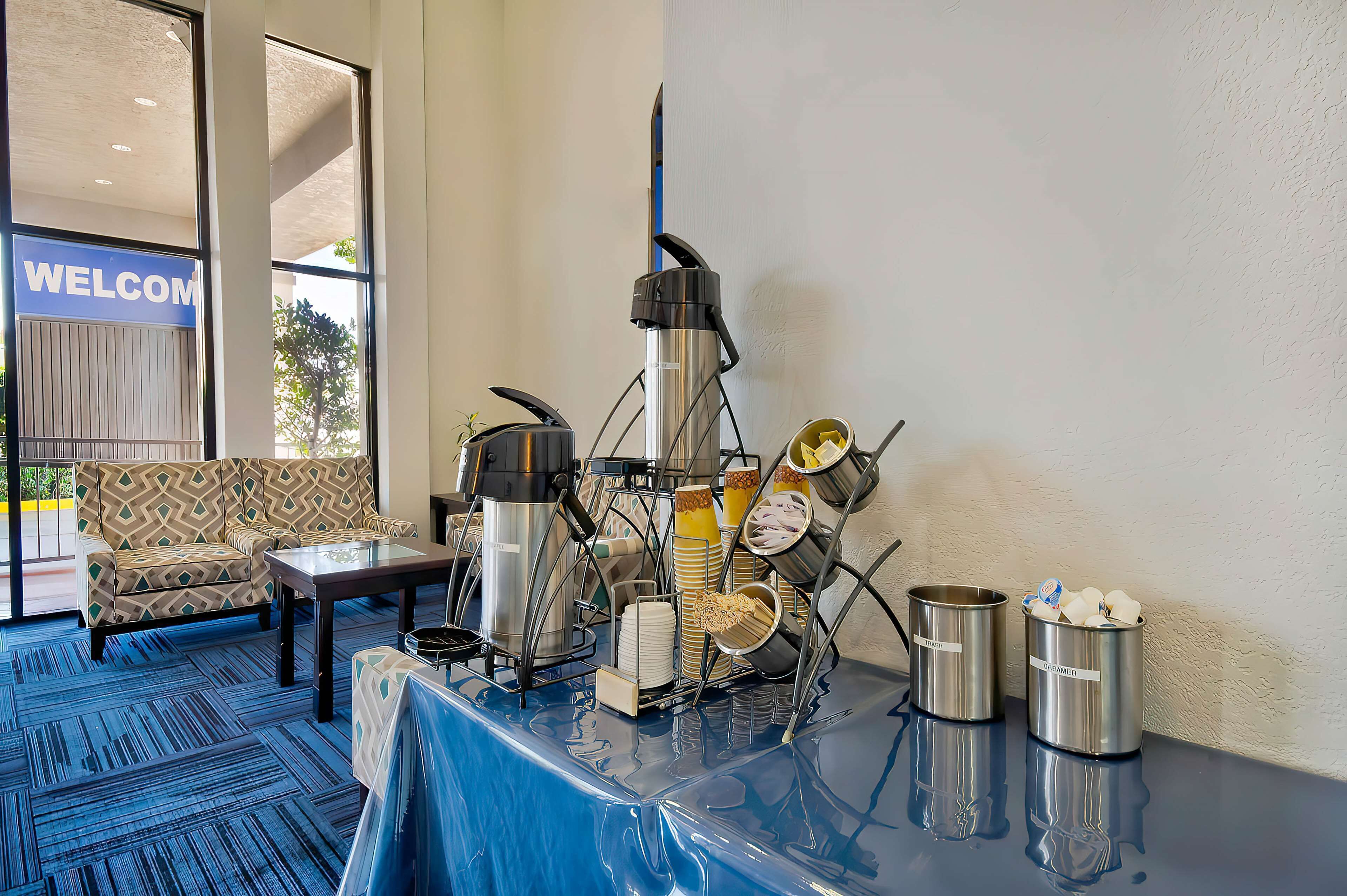 A breakfast buffet setup with a coffee machine, stacked plates, and condiment containers.
