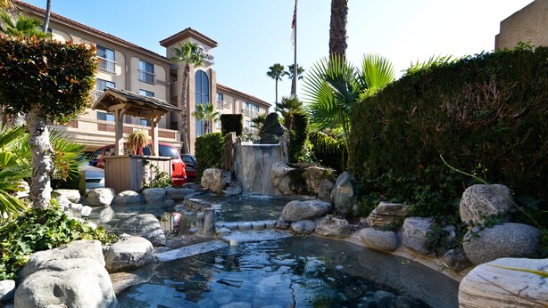 A courtyard with a small pond, rocks, and palm trees. - Studio 6 Suites Lawndale, CA – South Bay (Lawndale)