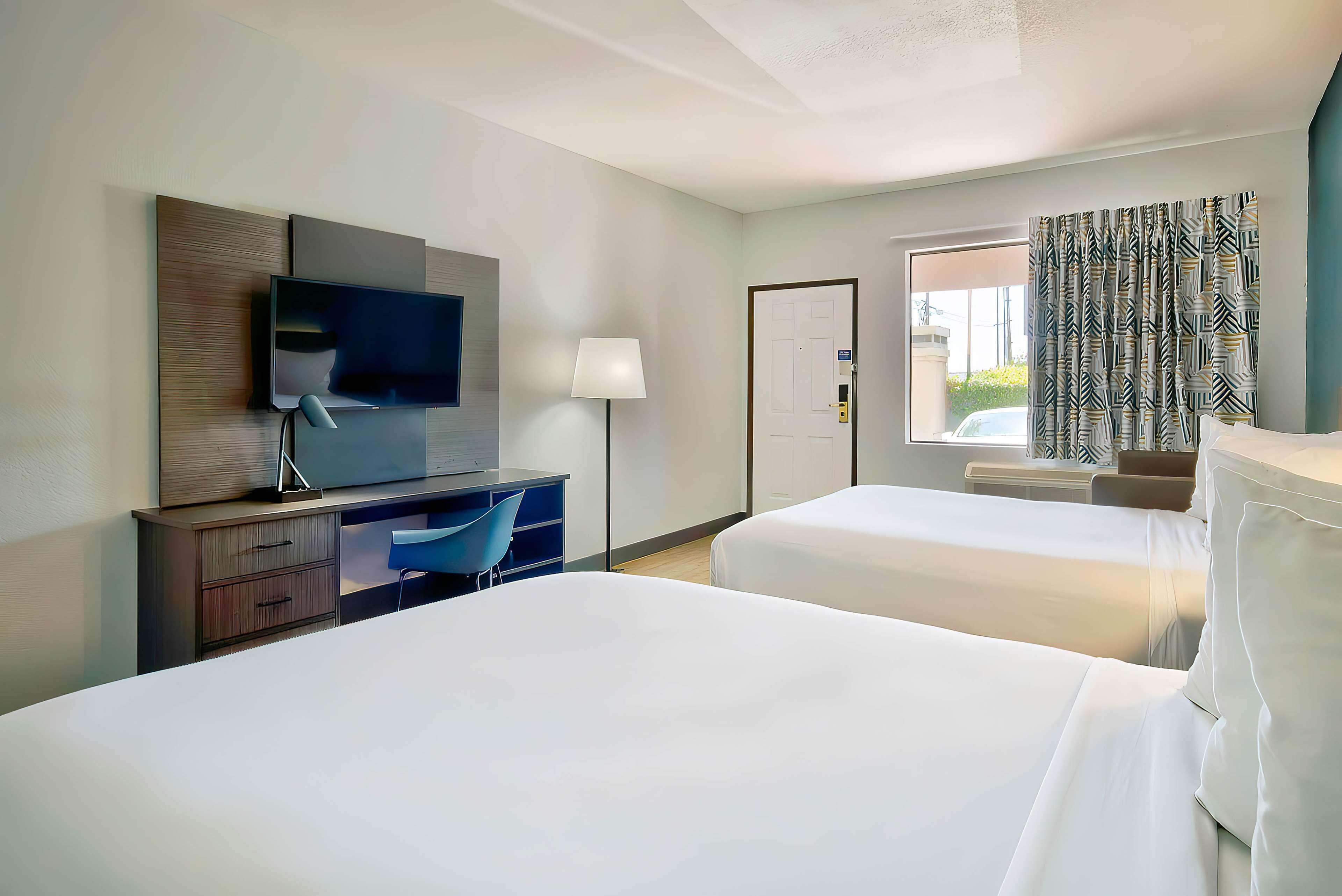 A hotel room with two beds, a desk with a chair, a TV, and a window with curtains.