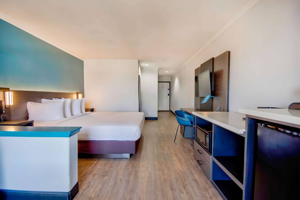 Ein Hotelzimmer mit Bett, Nachttisch, Schreibtisch, Stuhl und einem großen Spiegel.