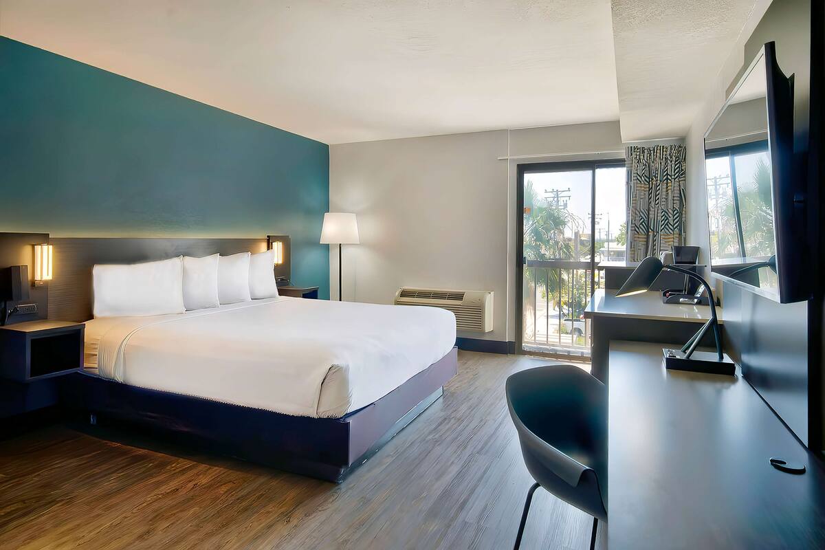 Ein modernes Hotelzimmer mit einem großen Bett, einem Schreibtisch, einem Sessel und einem Fernseher.