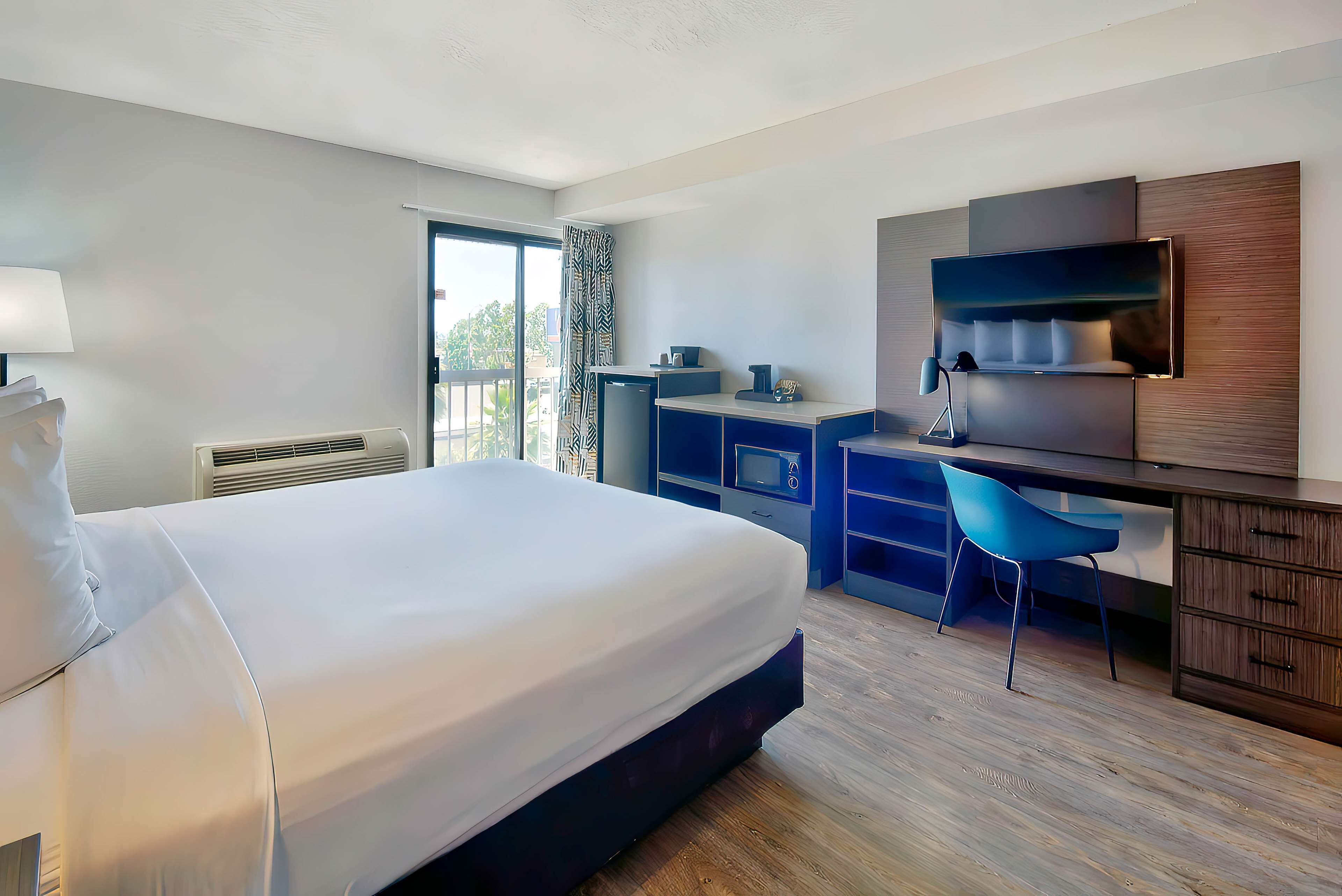 Una habitación de hotel moderna con una cama grande, un escritorio, una silla, un televisor y una ventana con cortinas.