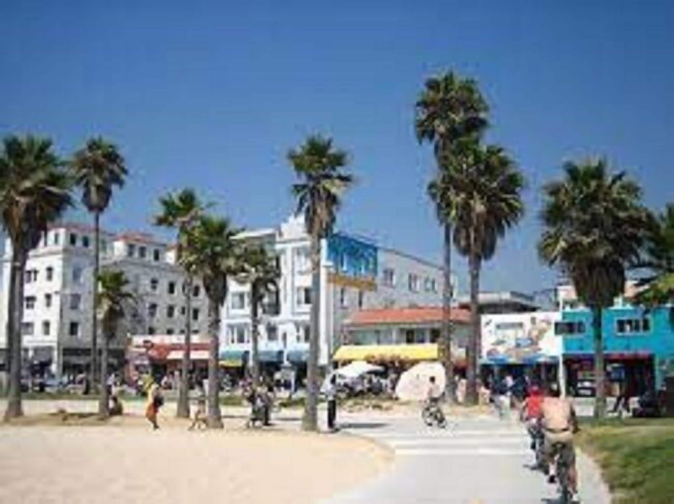 A beachfront promenade with palm trees, buildings, and people.