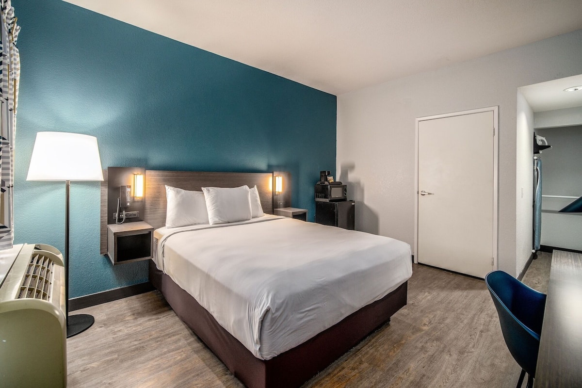 Une chambre d’hôtel avec un lit, des tables de chevet, une lampe, un four à micro-ondes et une porte.