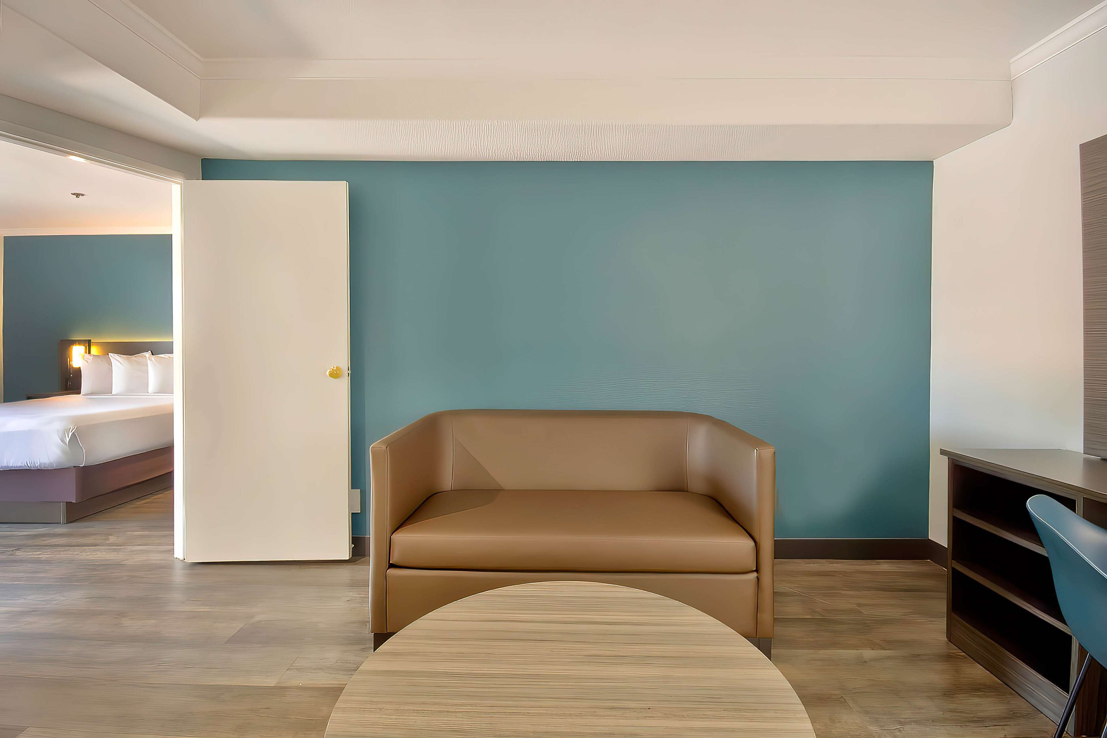 Una habitación de hotel moderna con un sofá de cuero marrón, una cama con sábanas blancas y una pared de acento color turquesa.