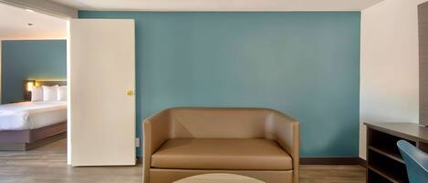 Una habitación de hotel moderna con un sofá de cuero marrón, una cama con sábanas blancas y una pared de acento color turquesa.