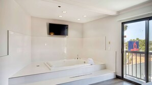 A modern bathroom with a freestanding bathtub, a mounted TV, and a large window providing a view of the outdoors. - Studio 6 Suites Lawndale, CA – South Bay (Lawndale)