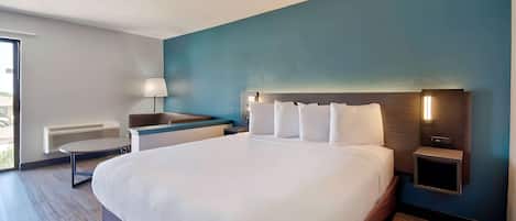 A modern hotel room with a large bed, bedside tables, a desk, and a lamp.