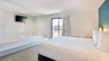 Una habitación de hotel moderna con una cama grande, una bañera integrada, un televisor de pantalla plana y un amplio ventanal con vistas al exterior.