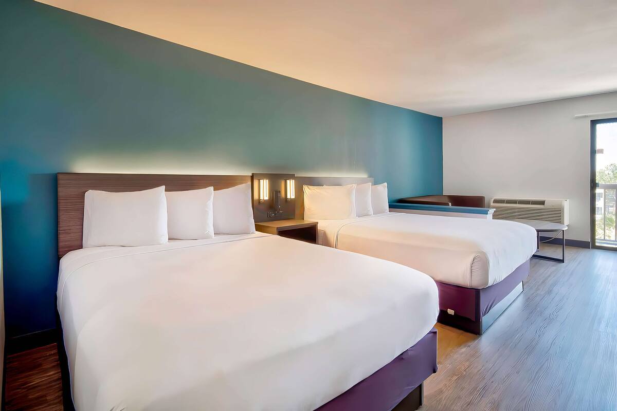 Ein Hotelzimmer mit zwei Betten, einem Nachttisch, einer Lampe und einem Fenster mit Blick.