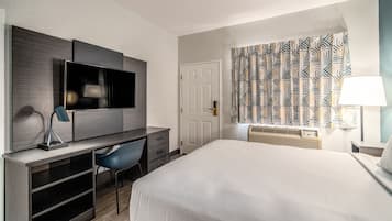 A hotel room with a bed, a desk with a chair, a television, and a patterned curtain.