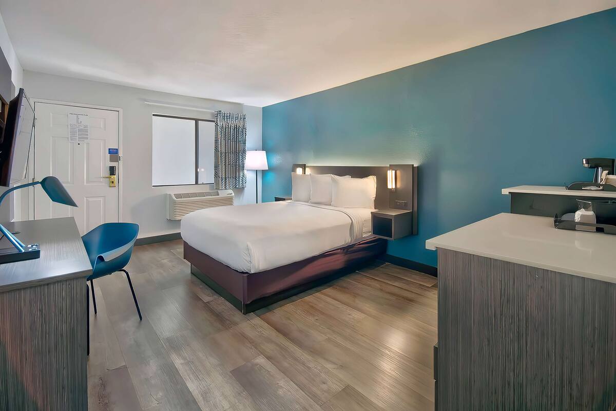 Ein Hotelzimmer mit Bett, Schreibtisch, Stuhl, Nachttisch und einem Fenster mit Vorhängen.