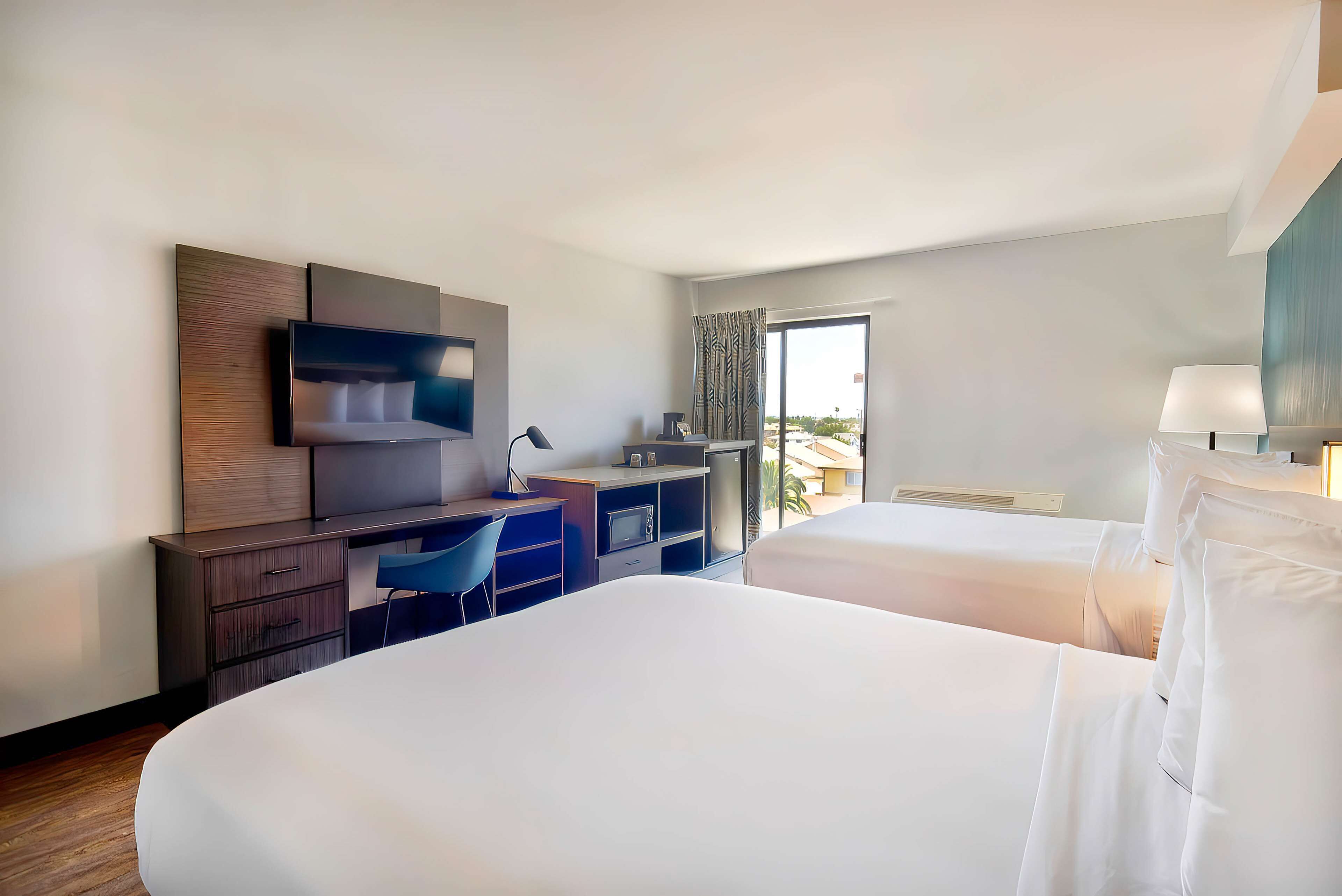 A hotel room with two beds, a desk, a chair, a TV, and a window with curtains.