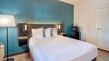 A hotel room with a large bed, bedside tables, a lamp, a phone, and a small shelf with items.