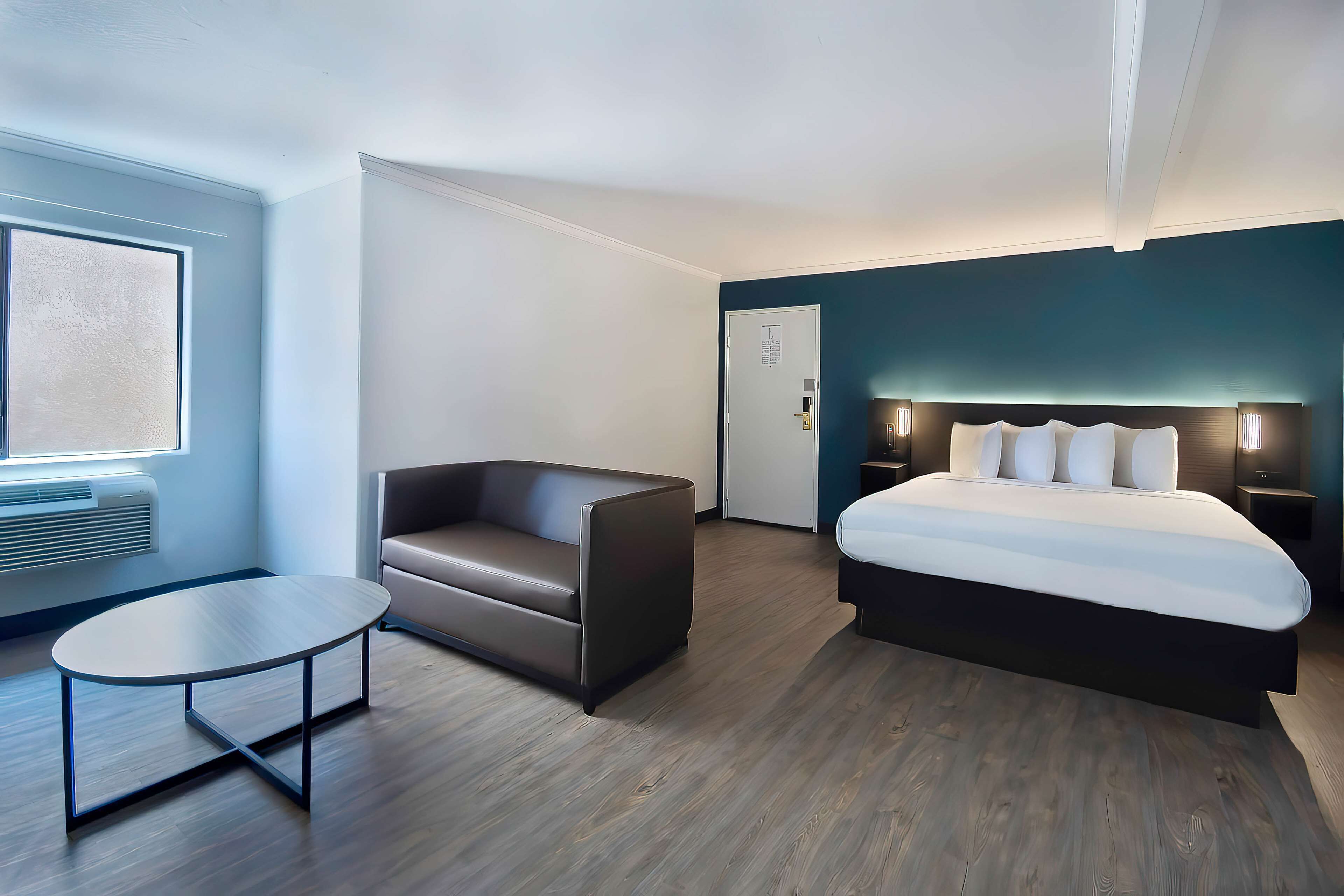 Une chambre d’hôtel moderne, équipée d’un lit, d’un canapé, d’une petite table et d’une fenêtre avec des stores.