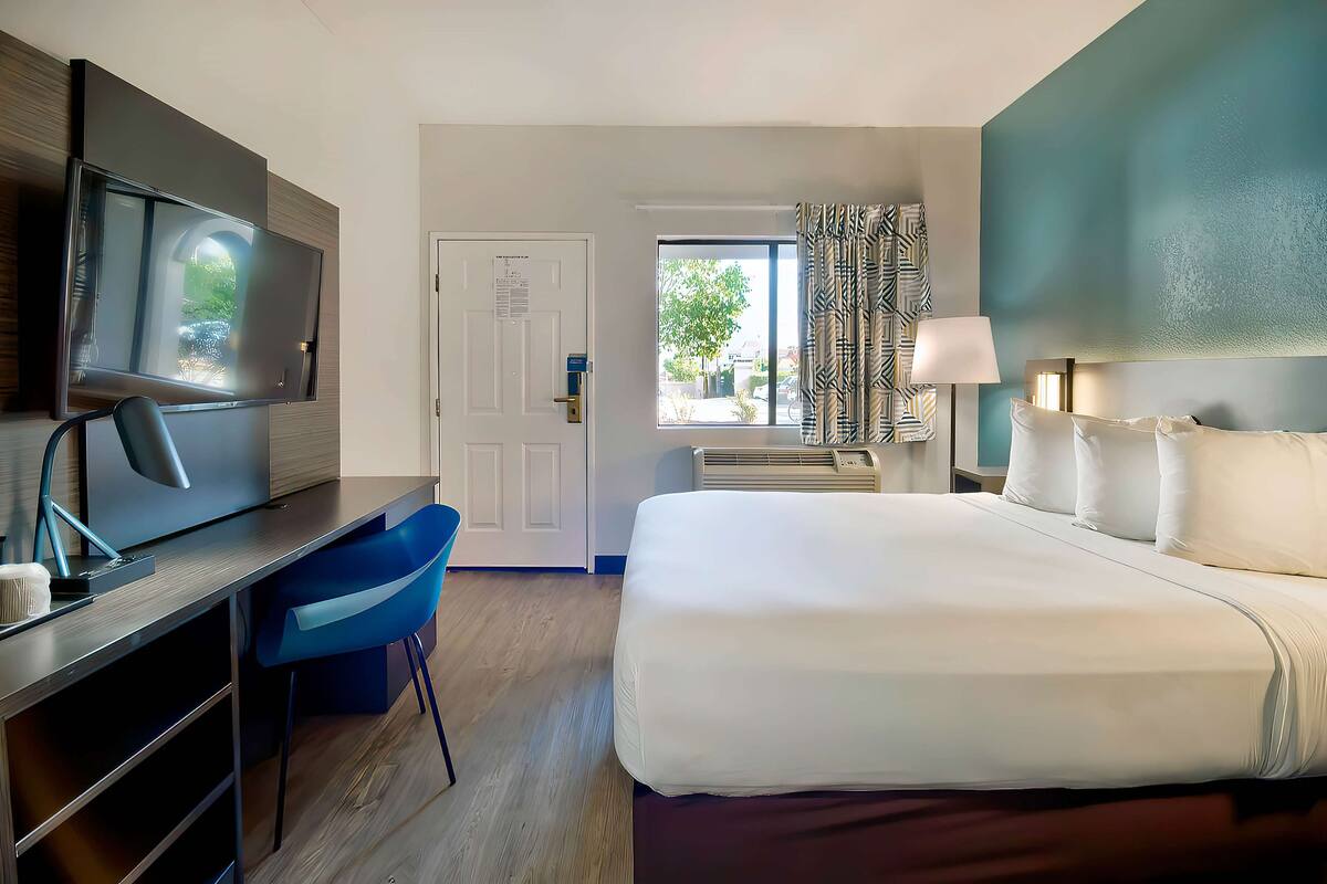 Ein Hotelzimmer mit Bett, Schreibtisch, Stuhl, Fernseher, Fenster und Vorhängen.