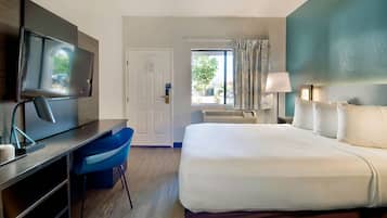 Habitación de hotel con cama, escritorio, silla, televisor, ventana y cortinas.