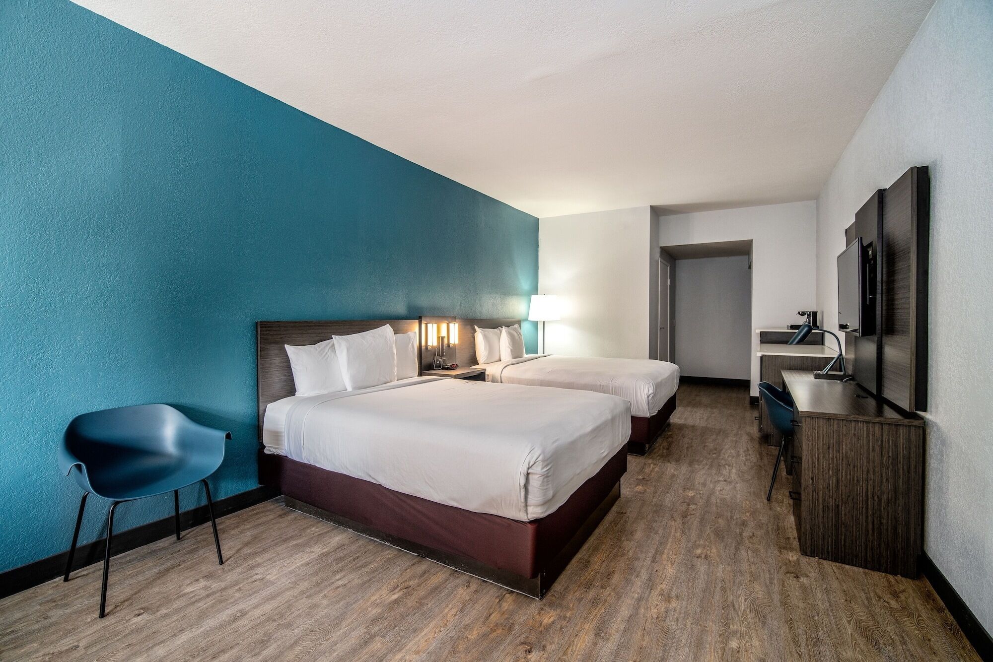 A hotel room with two beds, a desk, a chair, and a TV.