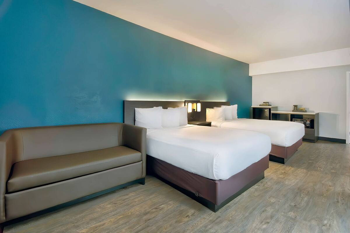 Ein Hotelzimmer mit zwei Betten, einem Schlafsofa, einem Schreibtisch und einem Nachttisch.