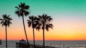A beach with palm trees, a pier, and the ocean at sunset. - Studio 6 Suites Lawndale, CA – South Bay (Lawndale)