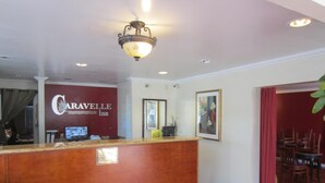 Un área de recepción con mostrador de madera, un letrero del Caravelle Inn, un televisor y un cuadro en la pared.