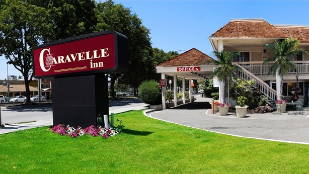 Un hotel con un letrero que dice "Caravelle Inn", que presenta un edificio de dos pisos con techo rojo, un área al aire libre techada y un estacionamiento.