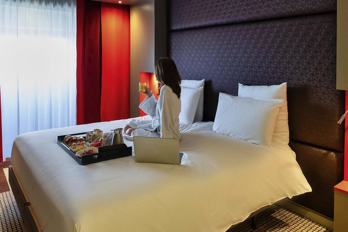 A hotel room with a large bed, white linens, a laptop, and a tray with breakfast items.