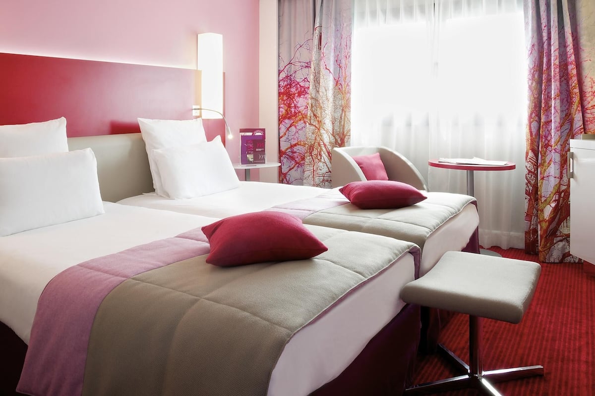 A hotel room with two beds, a small table, a chair, and a desk.