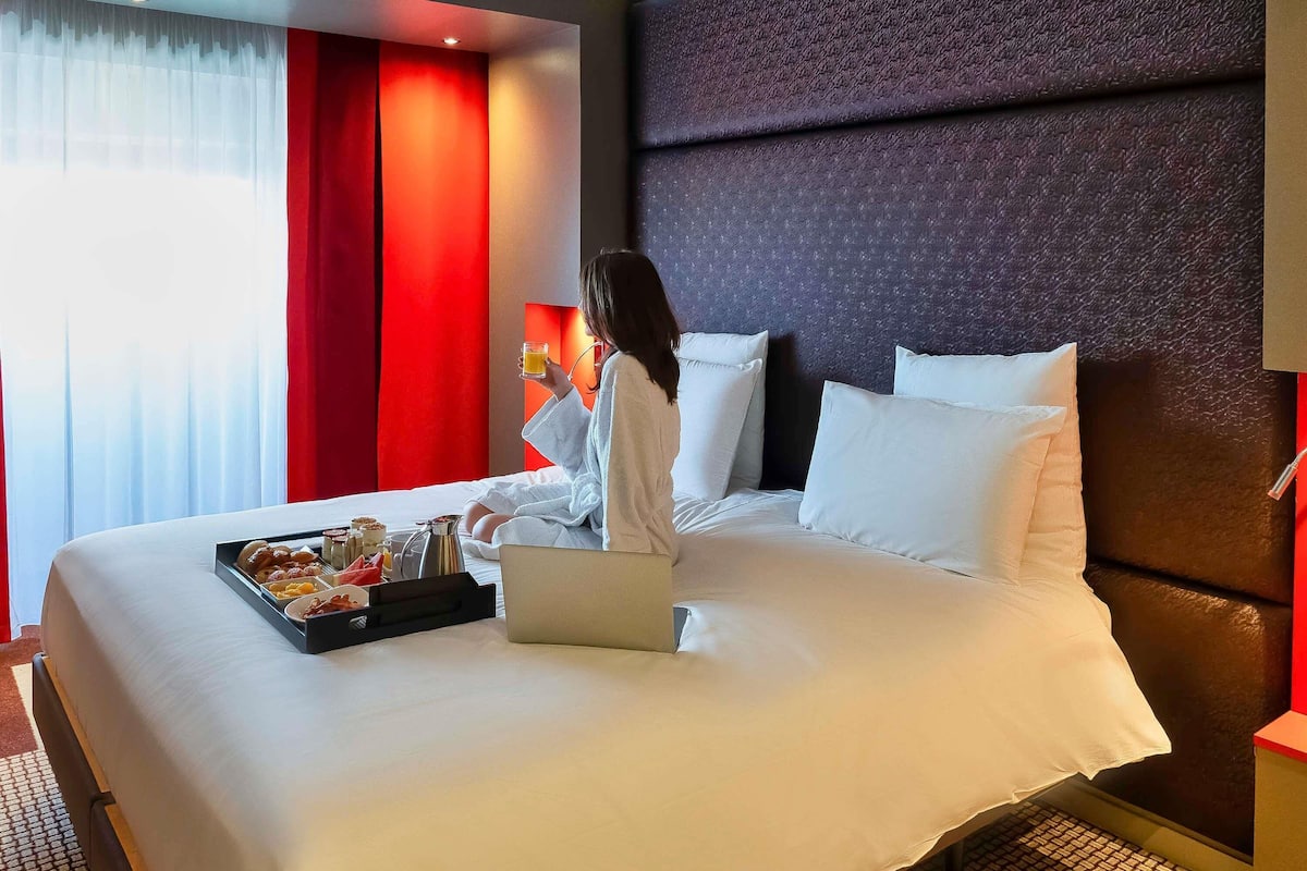 Habitación de hotel con una cama grande, una laptop, una bandeja de desayuno y una ventana con cortinas.