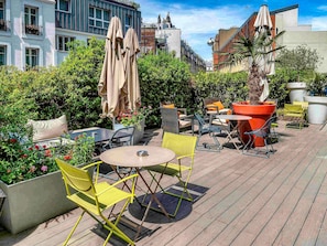 An outdoor patio with tables and chairs, surrounded by greenery and buildings. - Mercure Paris Montmartre Sacré Coeur (Paris)