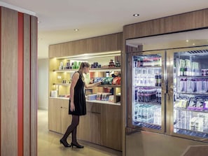 A woman in a black dress and heels standing in front of a refrigerated display case in a hotel lobby. - Mercure Paris Montmartre Sacré Coeur (Paris)