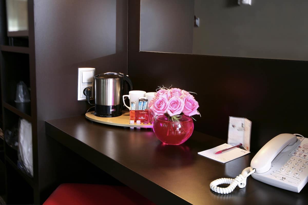 A hotel reception desk with a coffee maker, a vase of pink roses, a telephone, and a small card on the counter.