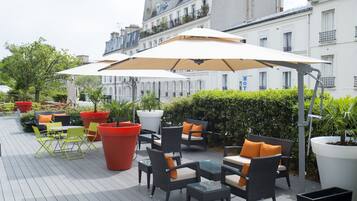 Eine Terrasses mit Korbmöbeln, großen Sonnenschirmen und Blumentöpfen.