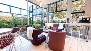 Een moderne buitenruimte met een glazen wand, een bar met krukken en uitzicht op de tuin.