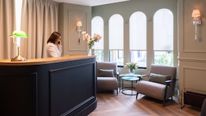 Un espace d’accueil avec un comptoir en bois, deux fauteuils, une petite table et un vase de fleurs.