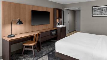 Una habitación de hotel con cama, escritorio, silla, televisor, cafetera y microondas.