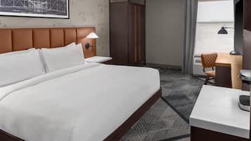 Une chambre d’hôtel avec un grand lit, un bureau avec une chaise, une lampe fixée au mur et une fenêtre avec des rideaux.