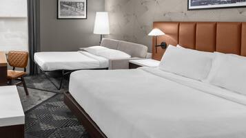A hotel room with a large bed, a smaller bed, a desk, a chair, and a lamp.